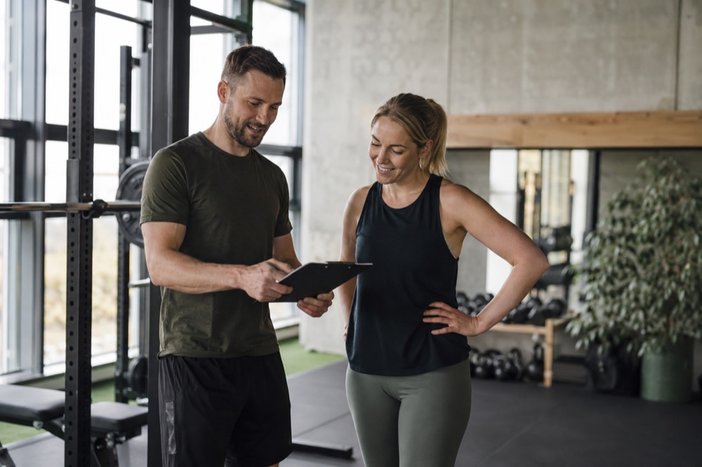 Personlig træner og klient gennemgår træningsplan sammen i et lyst fitnesscenter